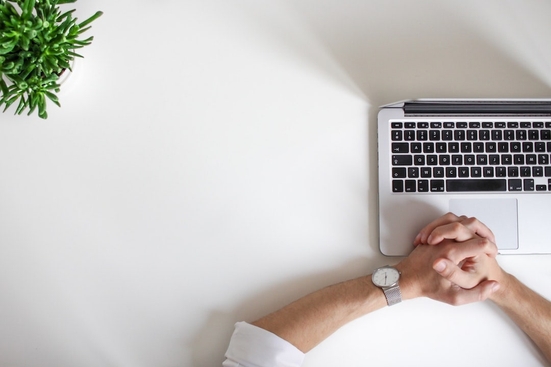 A professionally dressed person's hands folded over an open laptop