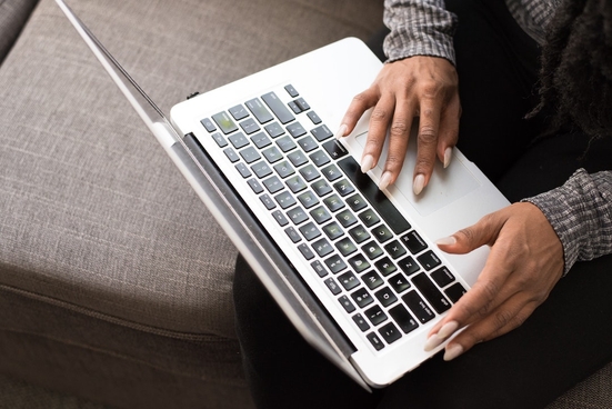 A woman with long fingernails typing on a silver laptop