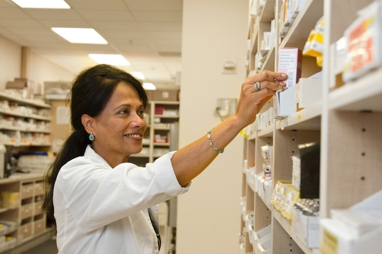 A middle-aged Indian woman reaches for a box in a pharmacy setting