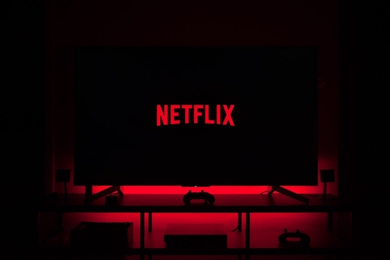 The Netflix logo on a black TV in a dark room with red downlighting. 
