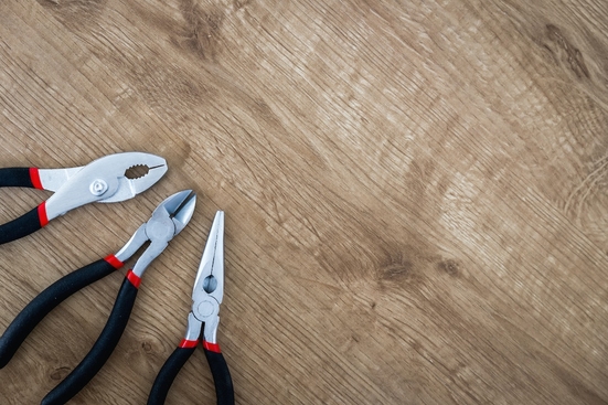 Three sets of pliers lined up on a pale wood background