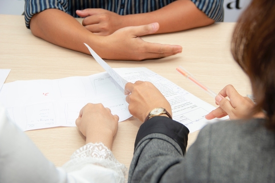 A close-up shot of two people viewing a printed resume across the table from an applicant with their arms loosely crossed