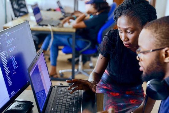 A Black man and Black woman looking intently at a laptop with code running on it.